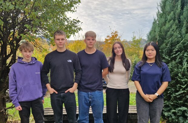 Schüler*innen stehen vor einer Bank mit grüner Landschaft im Hintergrund.