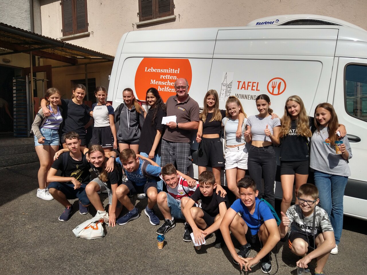 Foto von Schüler*innen und einer erwachsenen Person, die vor einem Wagen des Tafelladen Winnenden stehen.