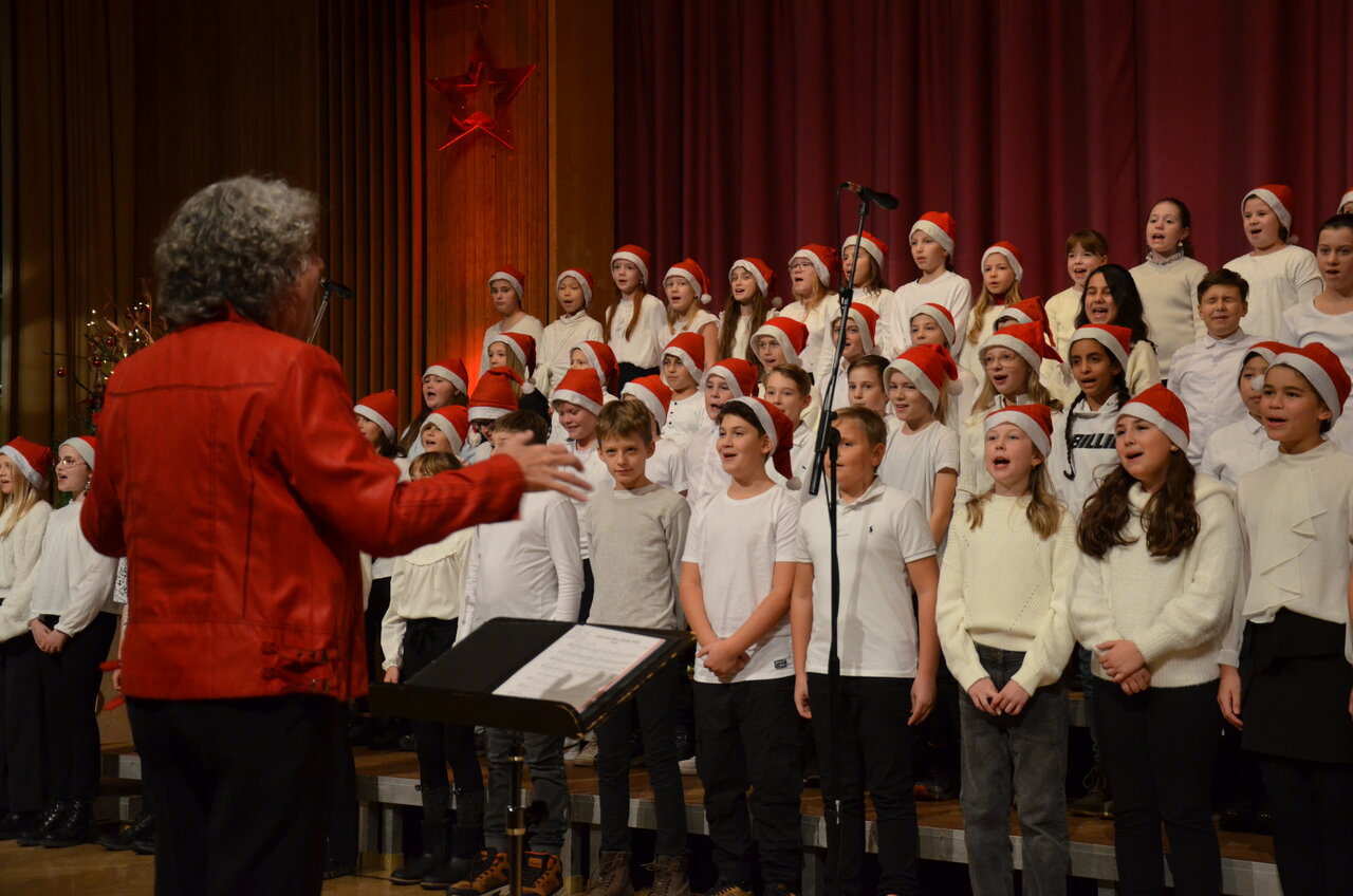 Ein singender Chor aus Schüler*innen mit Weihnachtsmützen auf.