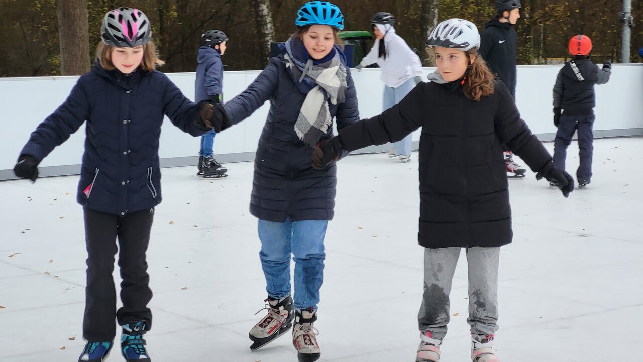 Foto von drei Mädchen, die Schlittschuhlaufen am Winteraktionstag und sich bei den Händen halten.