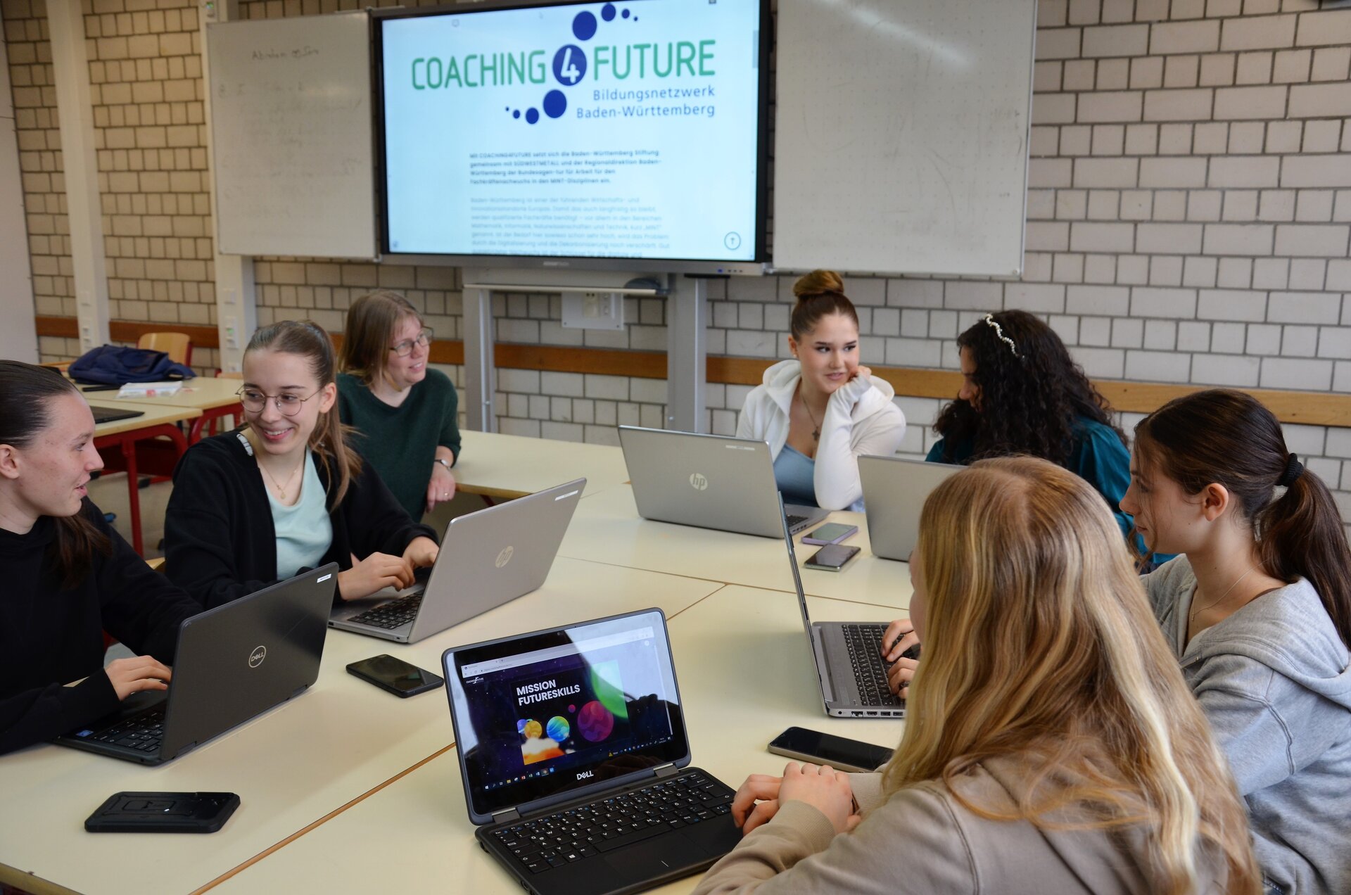 Foto von Schüler*innen, die an einem Tisch an Laptops arbeiten.