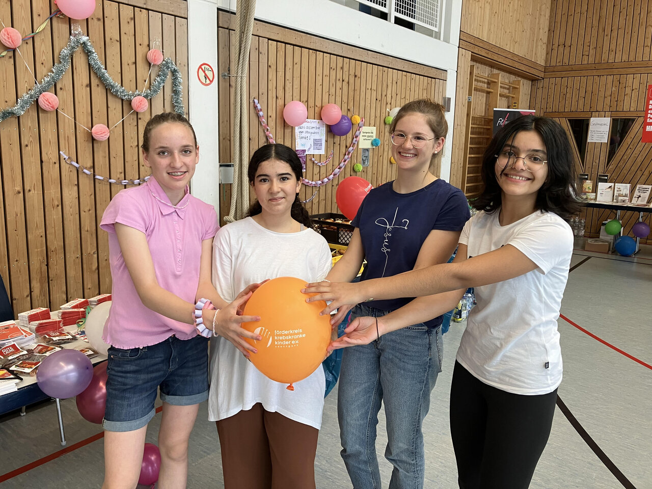 Vier schülerinnen, die in einem Festsaal gemeinsam einen Ballon halten.