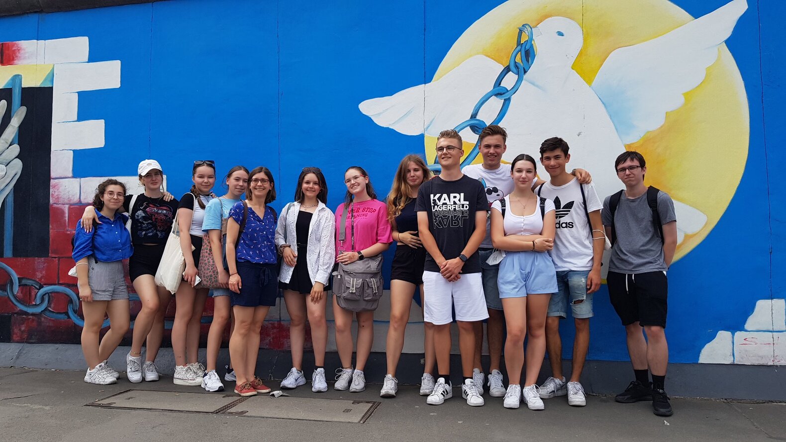 Schüler*innen, die vor einem Graffiti einer Friedenstaube auf der Berliner Mauer stehen.